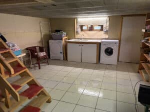 Buanderie de sous-sol avec carrelage clair, éclairage fluorescent, évier, sèche-linge et lave-linge Faure.