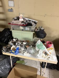 Table encombrée de nombreux paquets de cigarettes Lucky Strike Red, détritus, sacs poubelles noirs et boîte Urgo.