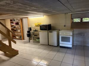 Cuisine de sous-sol carrelé avec étagères en bois, deux mini-frigos, un four/cuisinière blanche, et escalier en bois menant vers le haut.