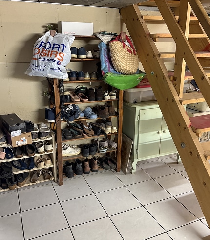 Rangement chaussures sous escalier et étagères Rangement chaussures et sacs sous escalier en bois, avec sac blanc 'PORT O'BIRS E.LECLERC'. Beaucoup de chaussures sur étagères en bois.