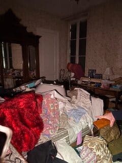 Chambre en désordre extrême : un fouillis impressionnant Chambre ancienne en désordre extrême. Vêtements accumulés sur le lit, couverture rouge, grande armoire et main avec porte-monnaie.